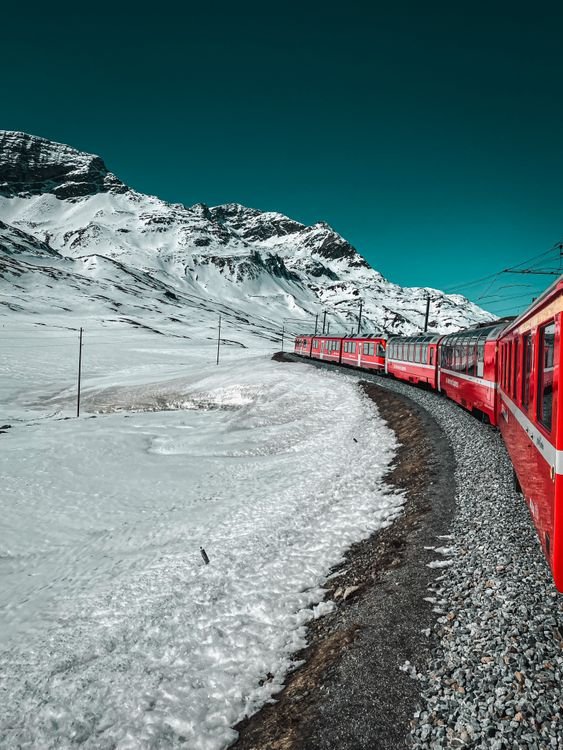 A red train travelling through snow-covered Alpine mountains